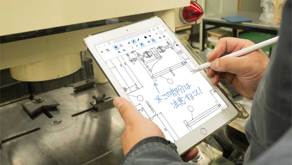 工場の作業員がタブレットに表示されている図面に文字を書いている様子