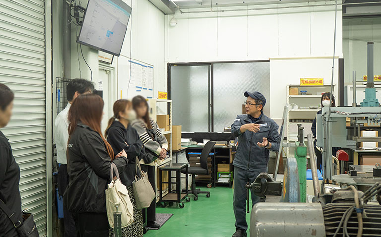 工場見学でアシストボードの画面を説明する工場長。参加者が注目している様子