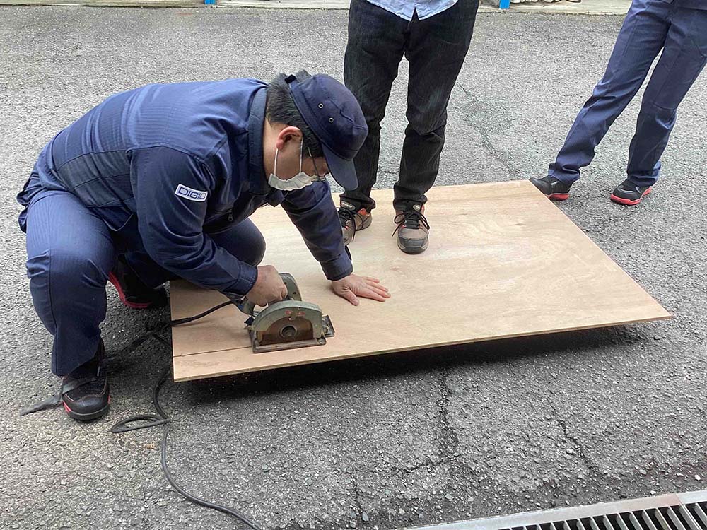 男性社員が丸ノコを使って、配管カバー用の木の板をカットしている様子。自分たちで材料を加工しています。