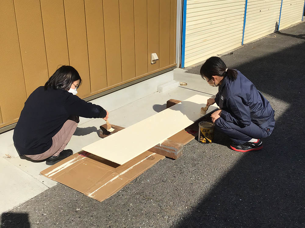 女性社員2名が協力して、カットした木の板にペンキを塗っている様子。丁寧に仕上げています。